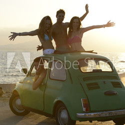 Group of happy friends with small car on the beach