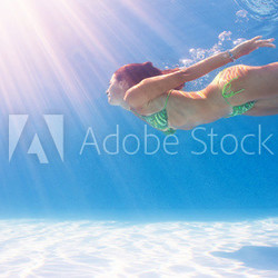 Woman swimming underwater in a blue pool.