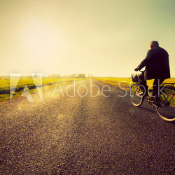 Old man riding a bike to sunny sunset sky