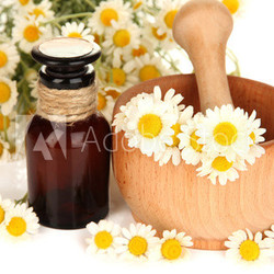 Essential oil and chamomile flowers in mortar close up
