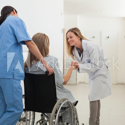 Doctor talking to patient in wheelchair while nurse is pushing